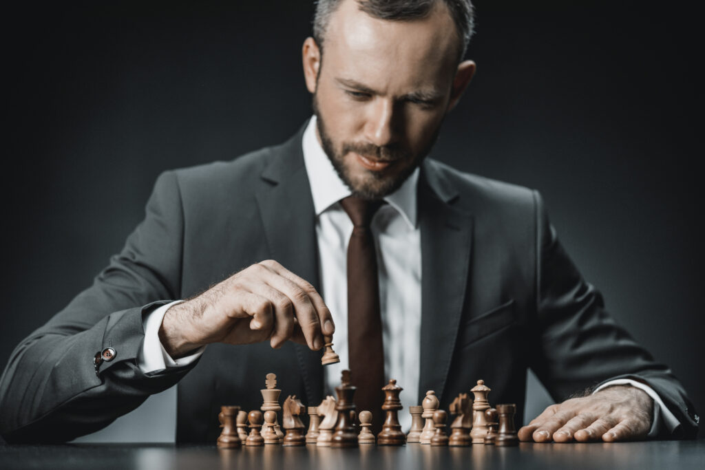 portrait of pensive businessman playing chess while sitting at table isolated on black